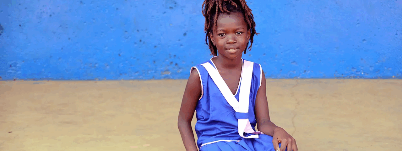 A girl poses for the photo wearing a blue dress, sitting in front of a blue wall