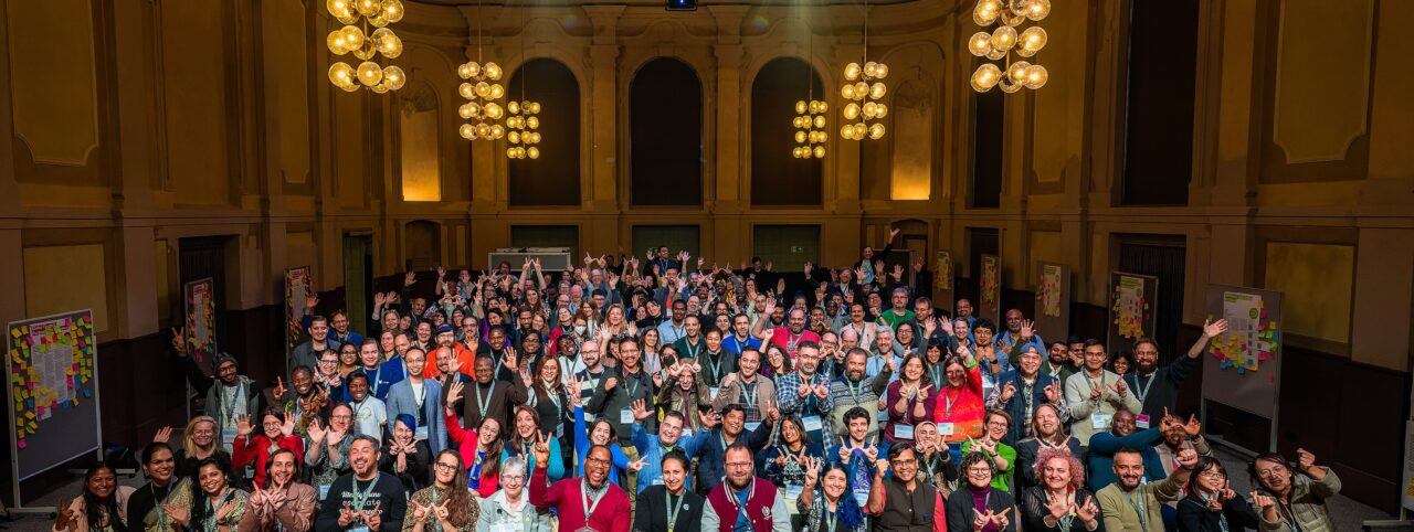 Group photo of participants in a large room at the Wikimedia Summit 2024